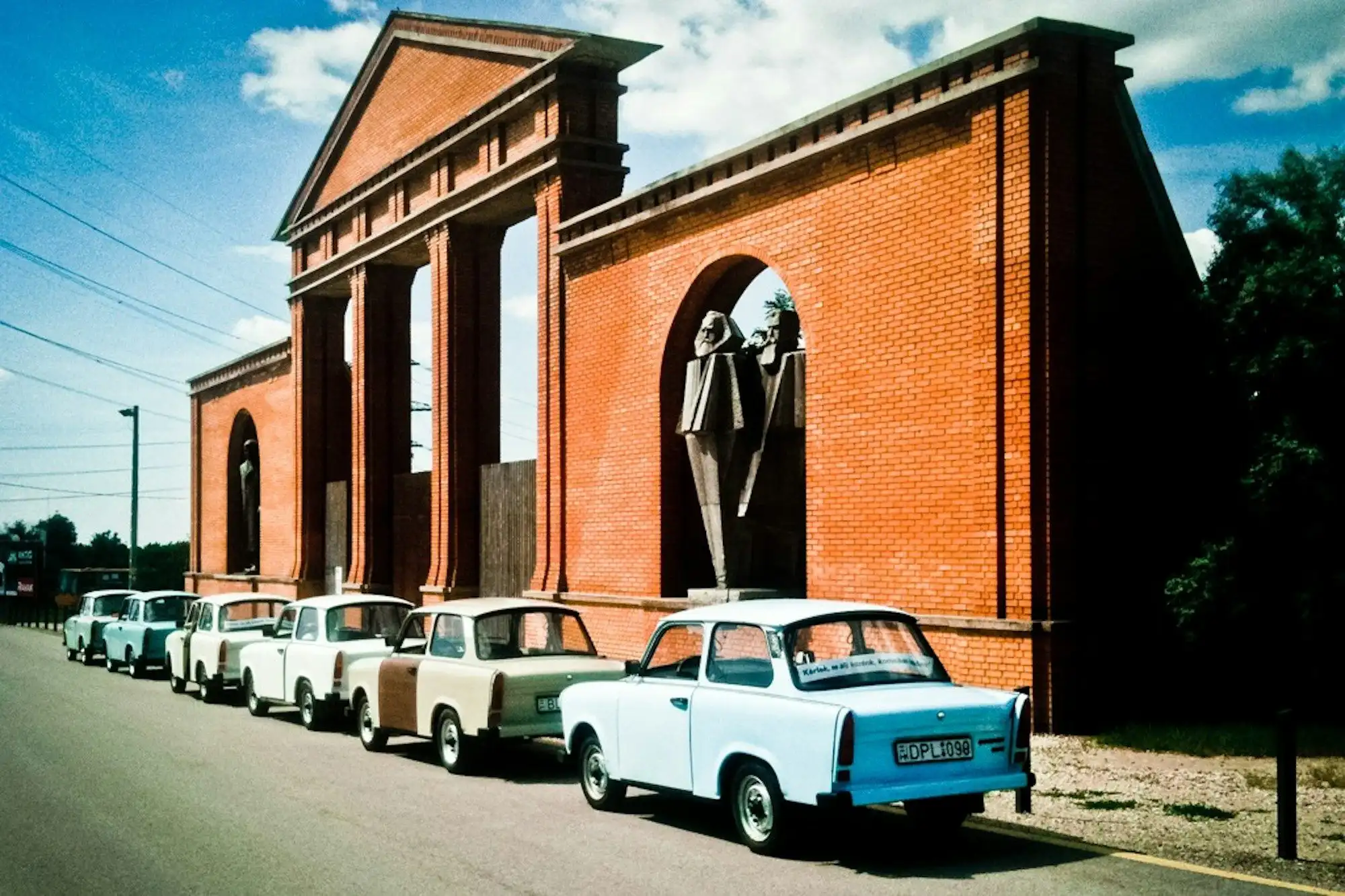 A row of Trabants parked outside the brick entrance facade of Memento Park