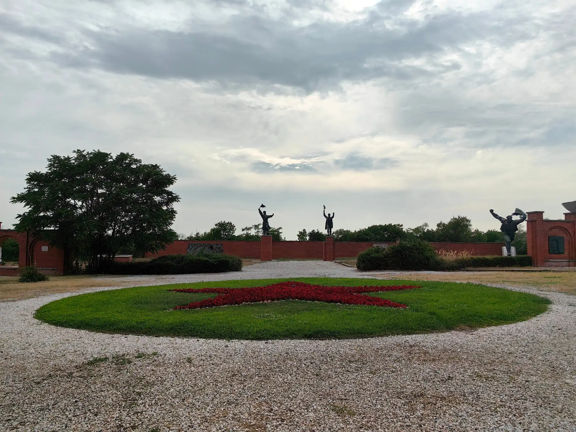 A wide view across the statue park at Memento Park, with the red-star flowerbed in the centre and statues along the brick walls