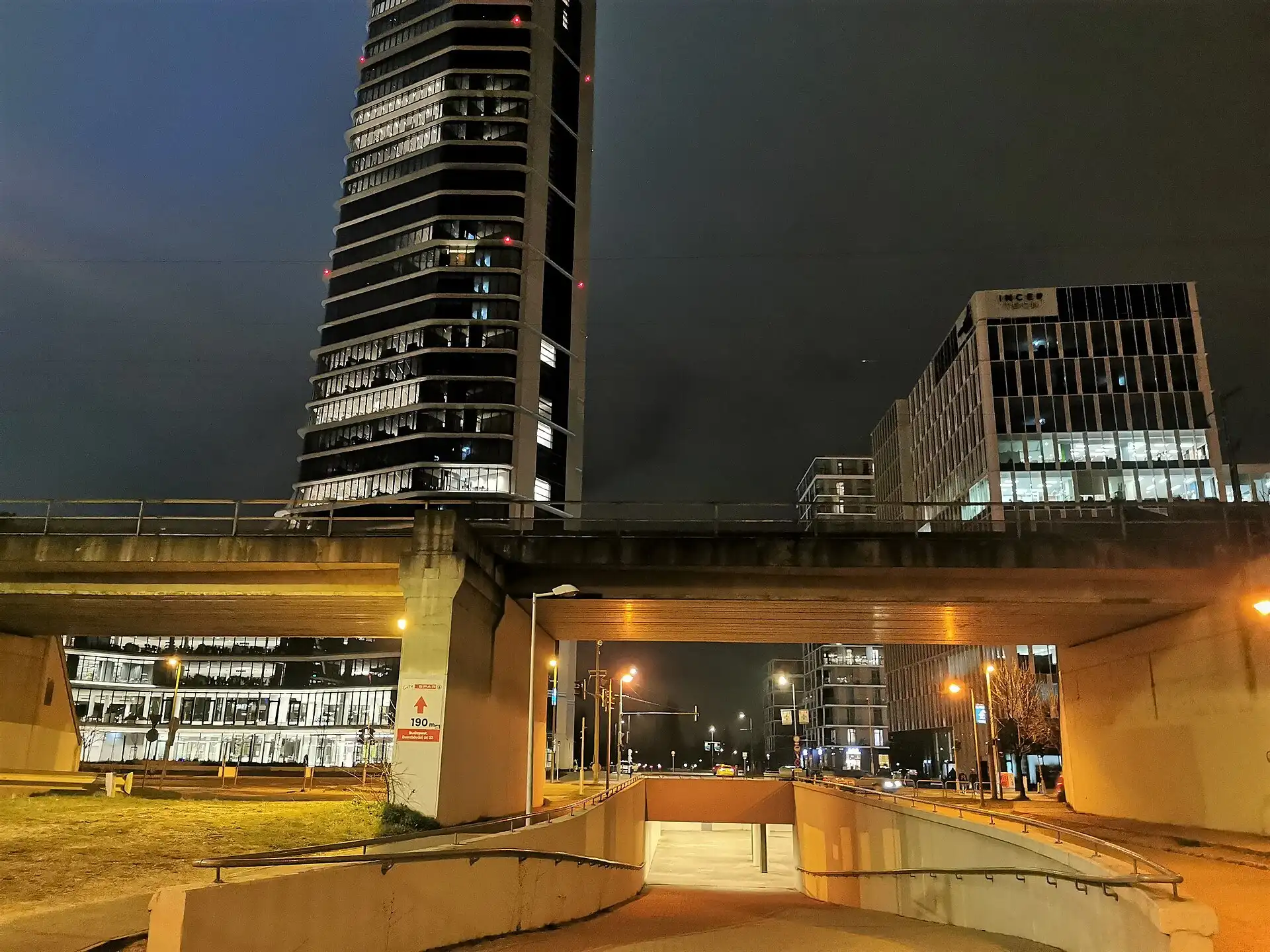 The MOL Campus tower in Budapest lit up at night, its curved glass flank rising above the surrounding buildings