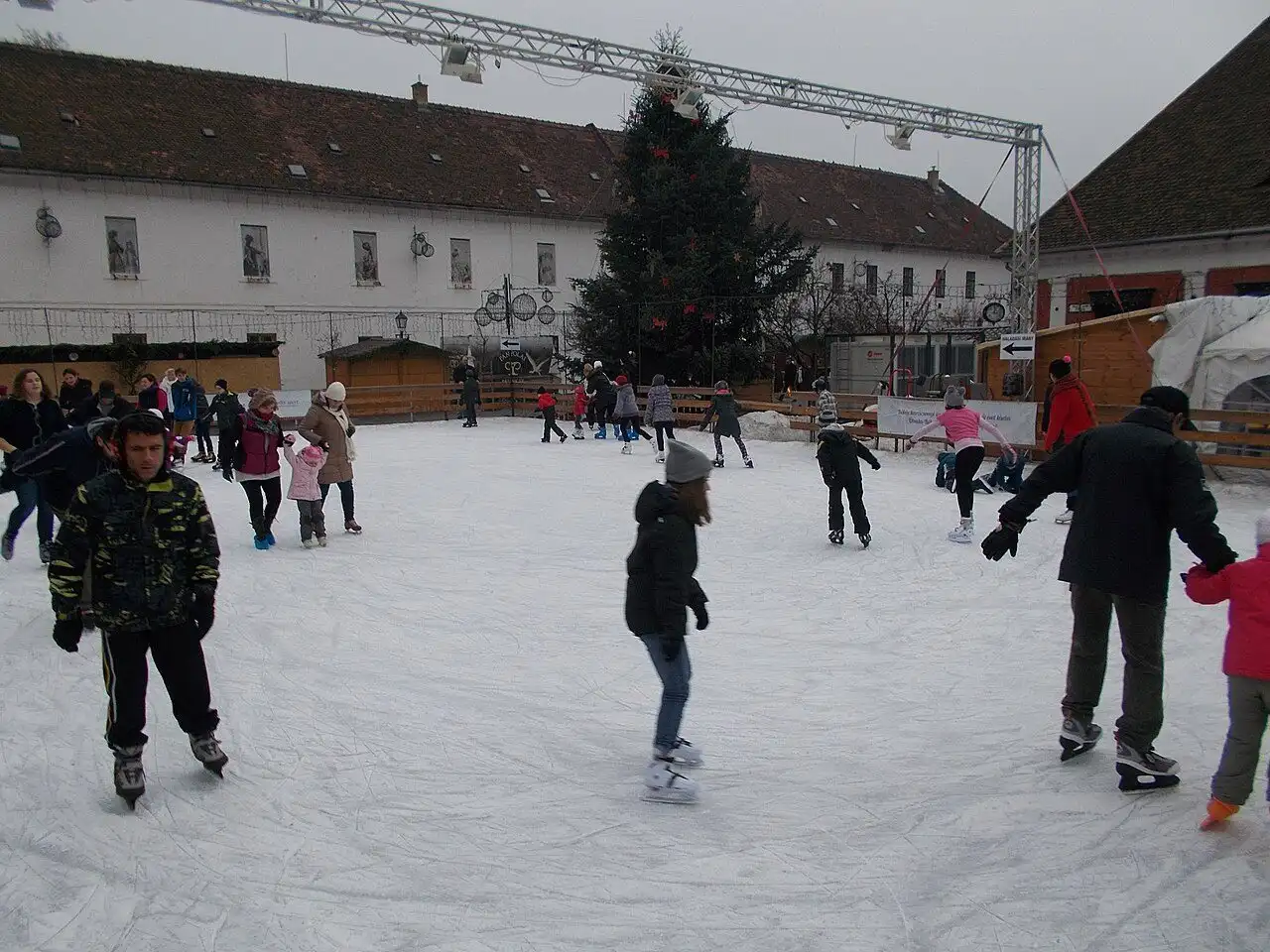 Families skating on the open-air rink on Fő tér in Óbuda in December, with the Christmas tree and a long white building behind