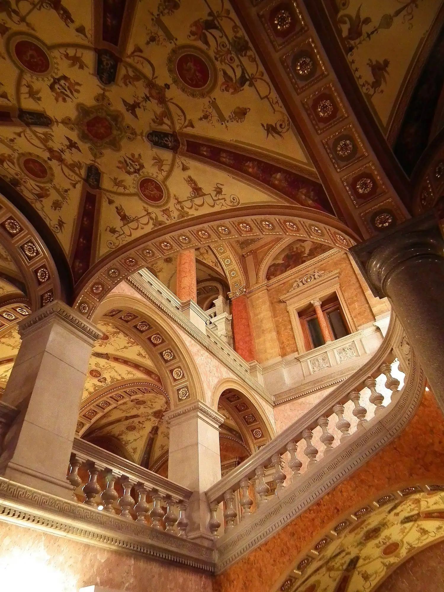 The grand staircase of the Hungarian State Opera House, with marble balustrades and painted vaulted ceilings above