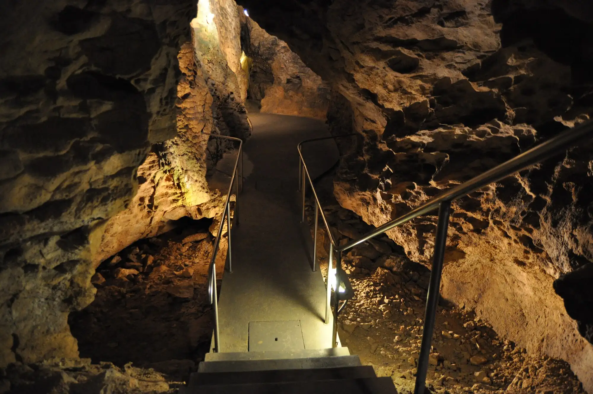 A lit passage inside the Pál-völgyi Cave in Budapest, with metal steps and a handrail running between pale rock walls