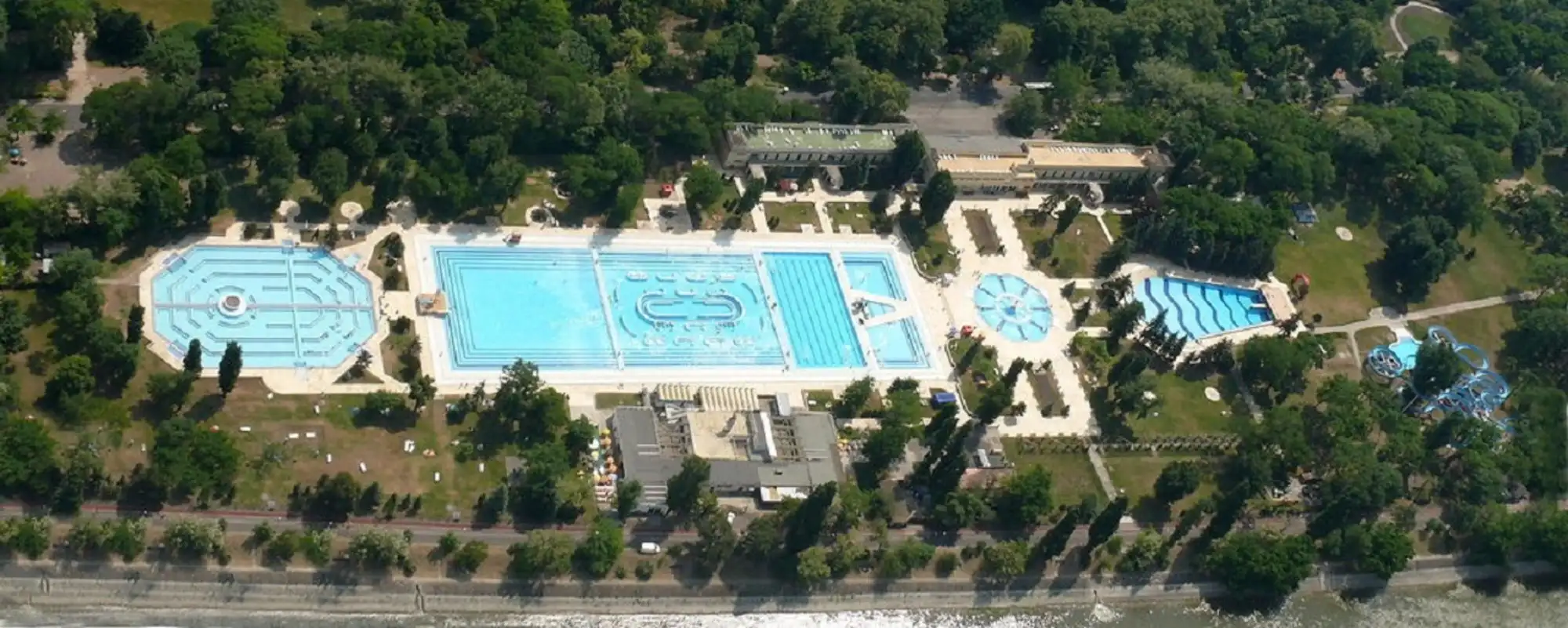 Aerial view of the outdoor pools at Palatinus, with the long lane pool in the middle, the polygonal pools either side and the trees of Margaret Island around them