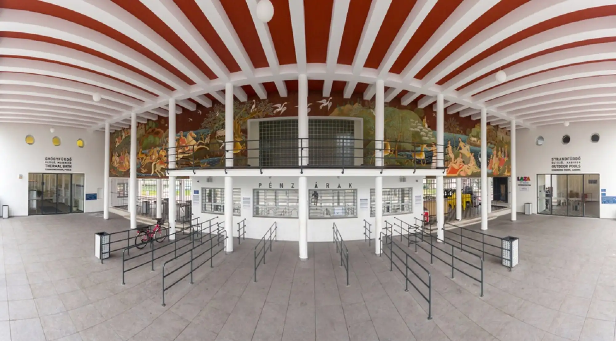 The entrance hall at Palatinus, a white hall with a red and white ribbed ceiling, a painted mural above the row of ticket windows and queue barriers in front