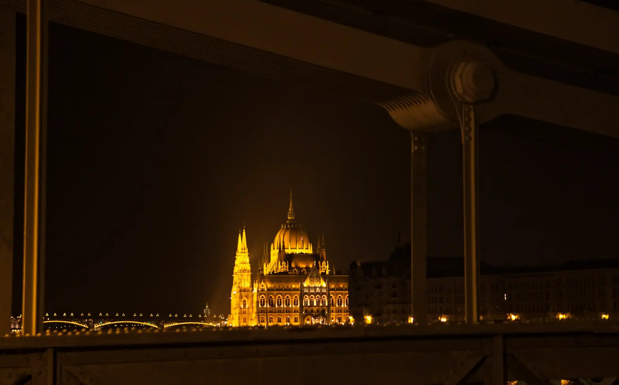 The floodlit dome of the Hungarian Parliament framed by the ironwork of the Chain Bridge at night