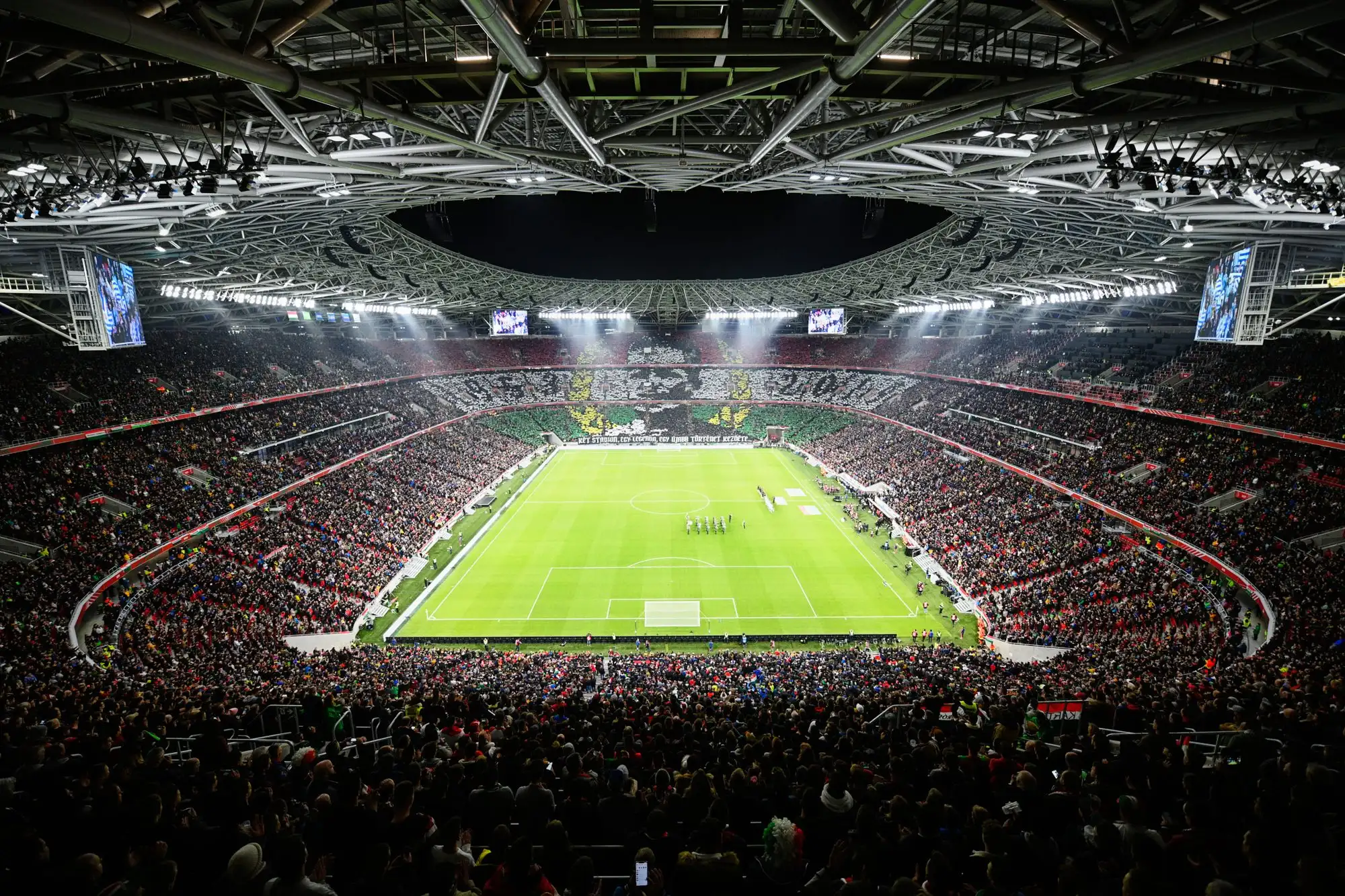 Puskás Aréna full for a night match, the stands lit and the pitch bright under the floodlights