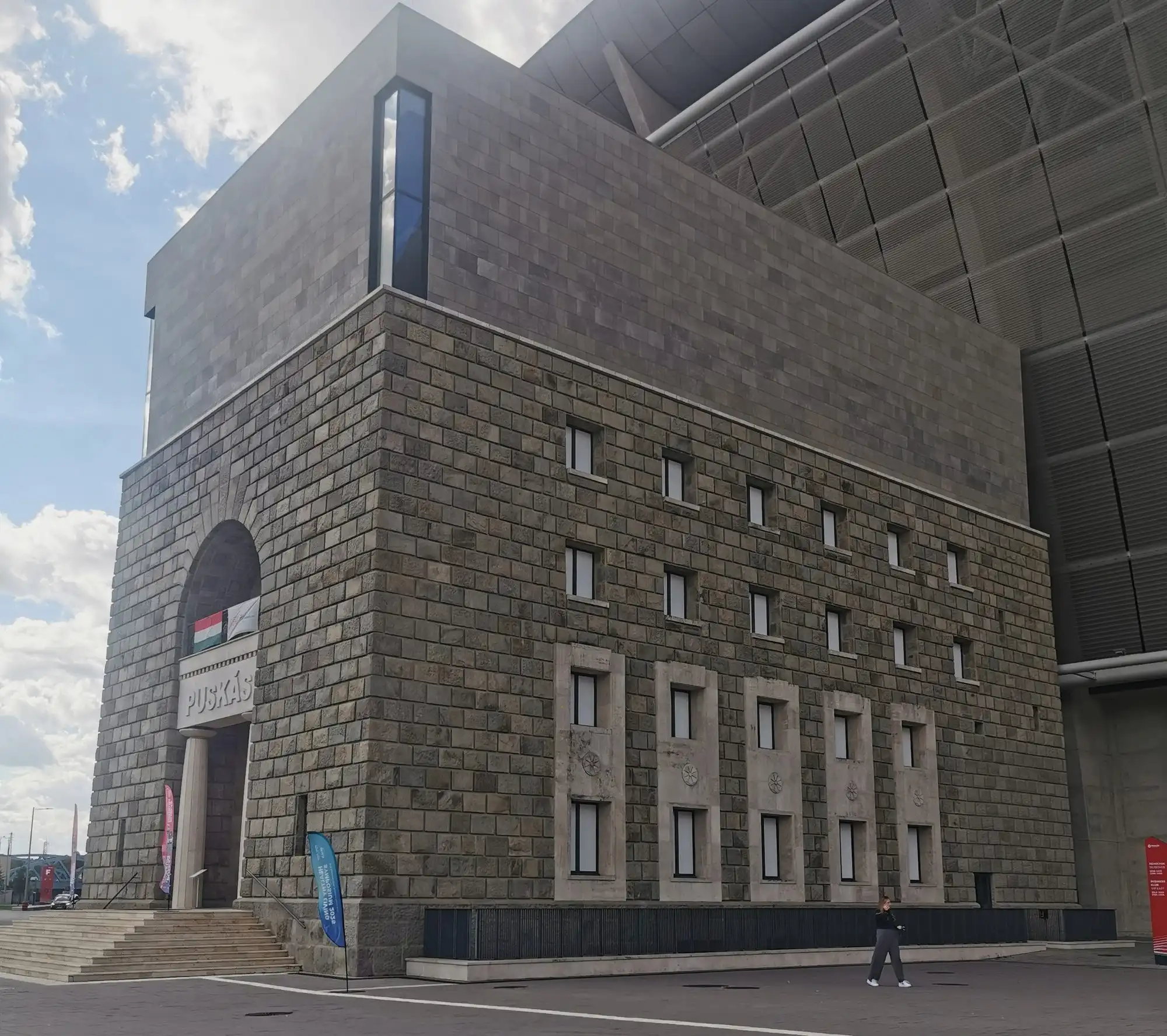 The stone-clad Tower building of the old Népstadion, now the Puskás Museum, with the new stadium's roof behind it