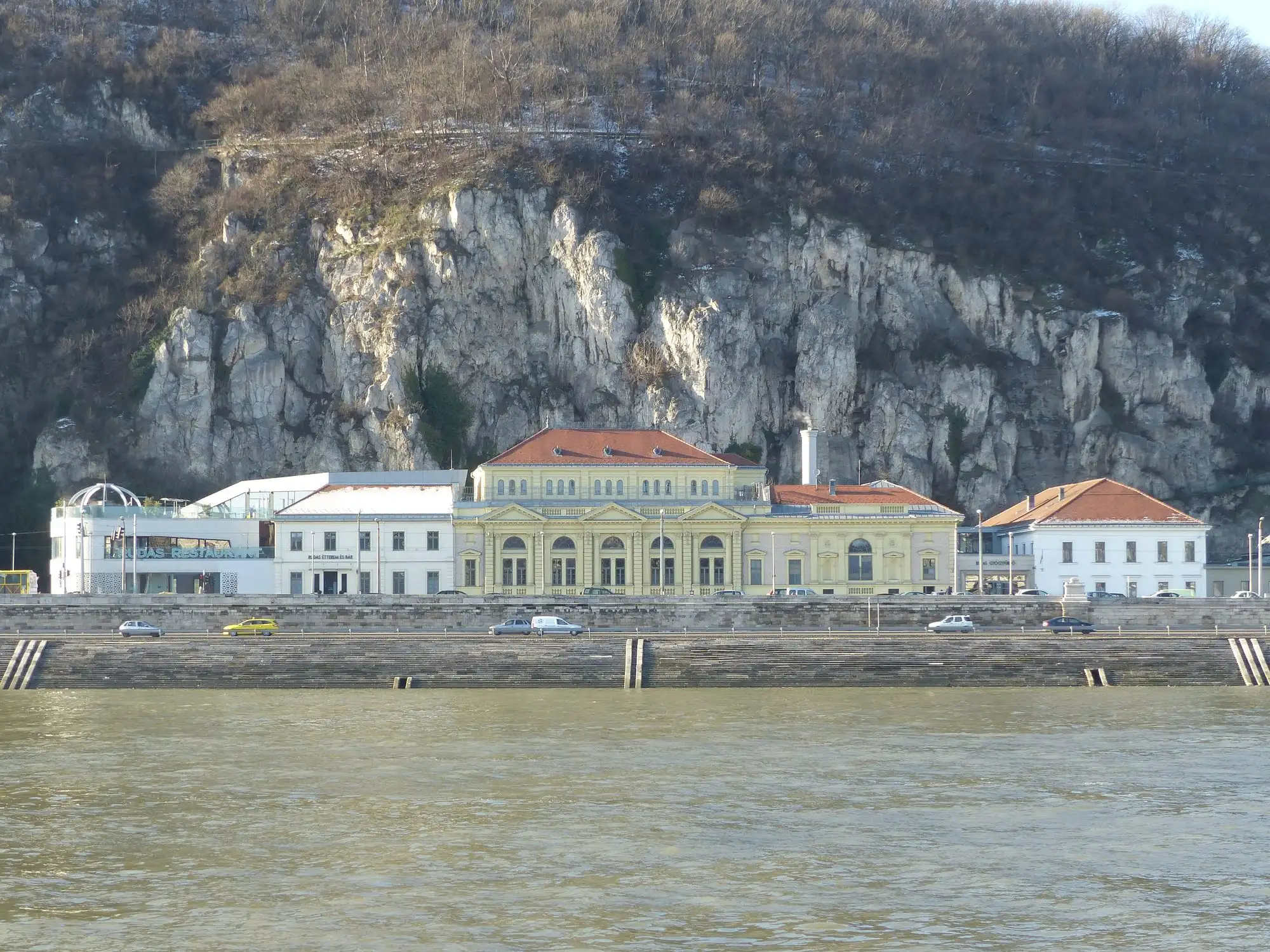 Rudas Thermal Bath seen across the Danube, a long yellow building on the Buda embankment below the cliffs of Gellért Hill