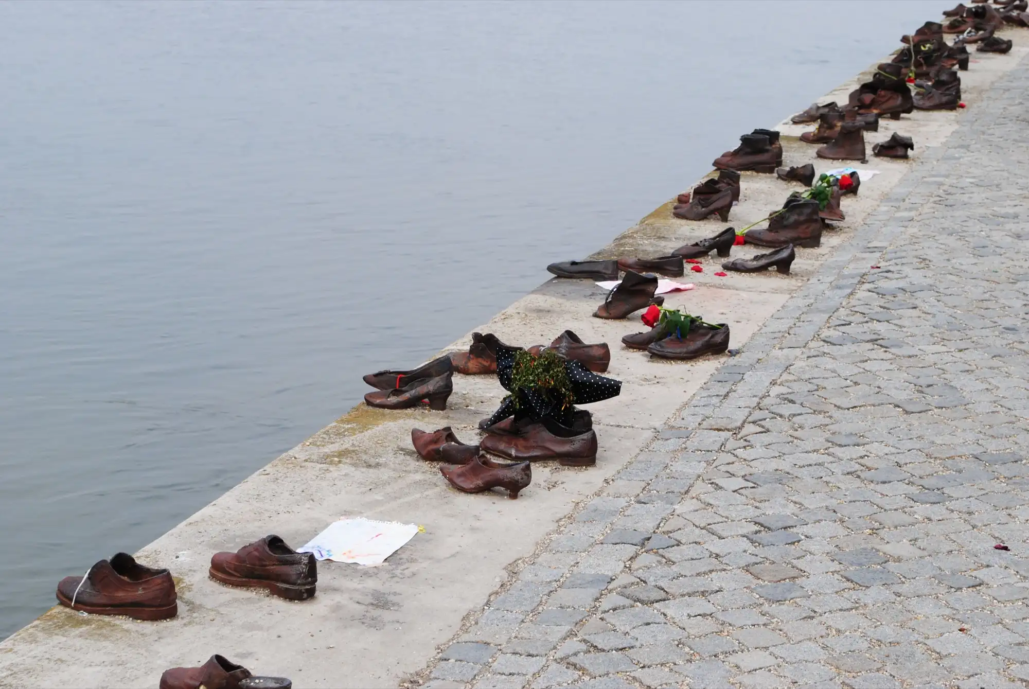 Rows of cast-iron shoes along the stone edge of the Danube embankment in Budapest, some holding flowers