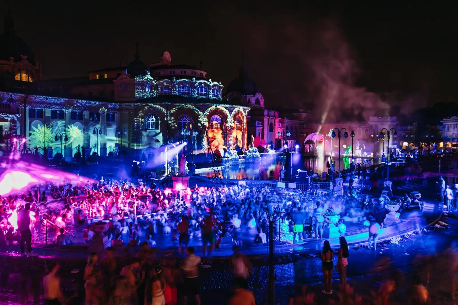 Sparty at Széchenyi Thermal Bath: a crowd in the outdoor pool under purple and blue lights, with projections across the floodlit bath building