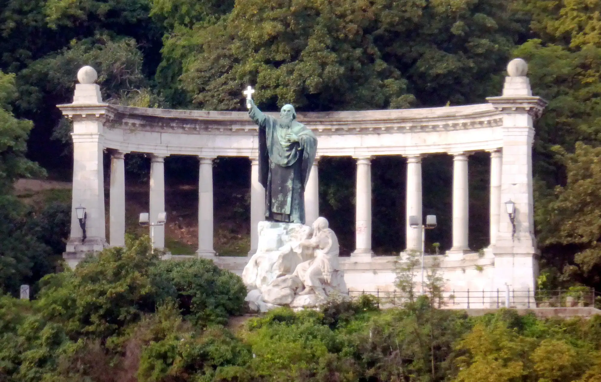 The bronze statue of Bishop Gellért raising a cross, standing in front of its semicircular colonnade on the hillside of Gellért Hill