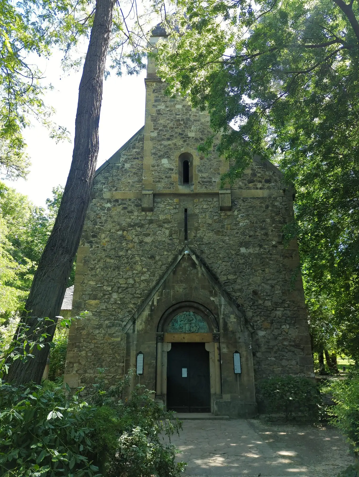 The stone west front of Saint Michael's chapel on Margaret Island, with its pointed doorway, bell tower and a bronze relief above the door
