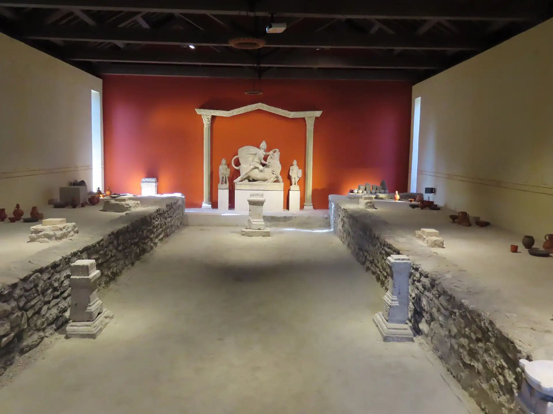 Inside the reconstructed Symphorus mithraeum at Aquincum, with the sculpture of Mithras and the bull lit against a red wall and low stone benches down both sides