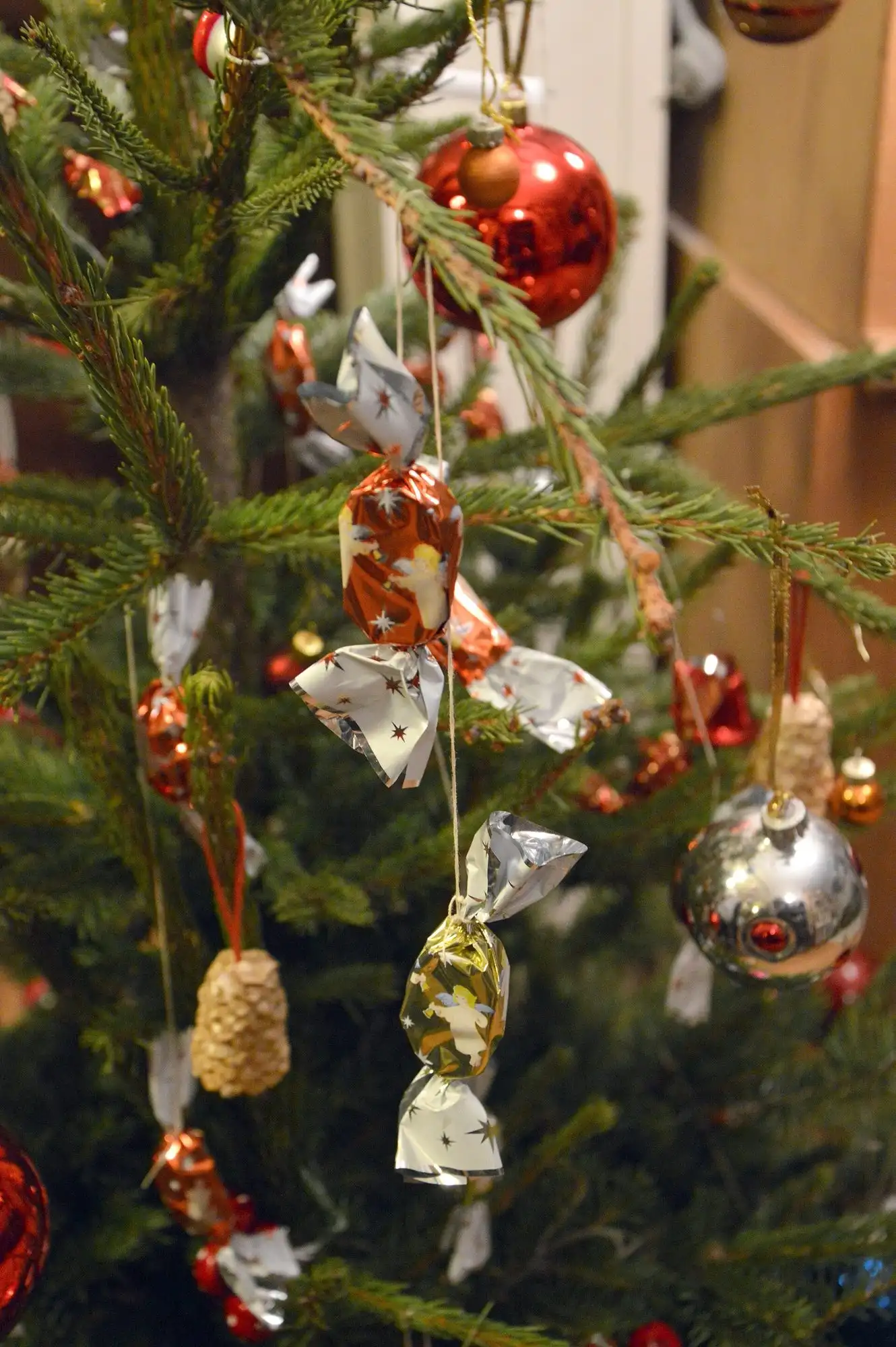 Szaloncukor sweets in silver and orange fringed wrappers hanging on the branches of a real Christmas tree, among red and silver baubles