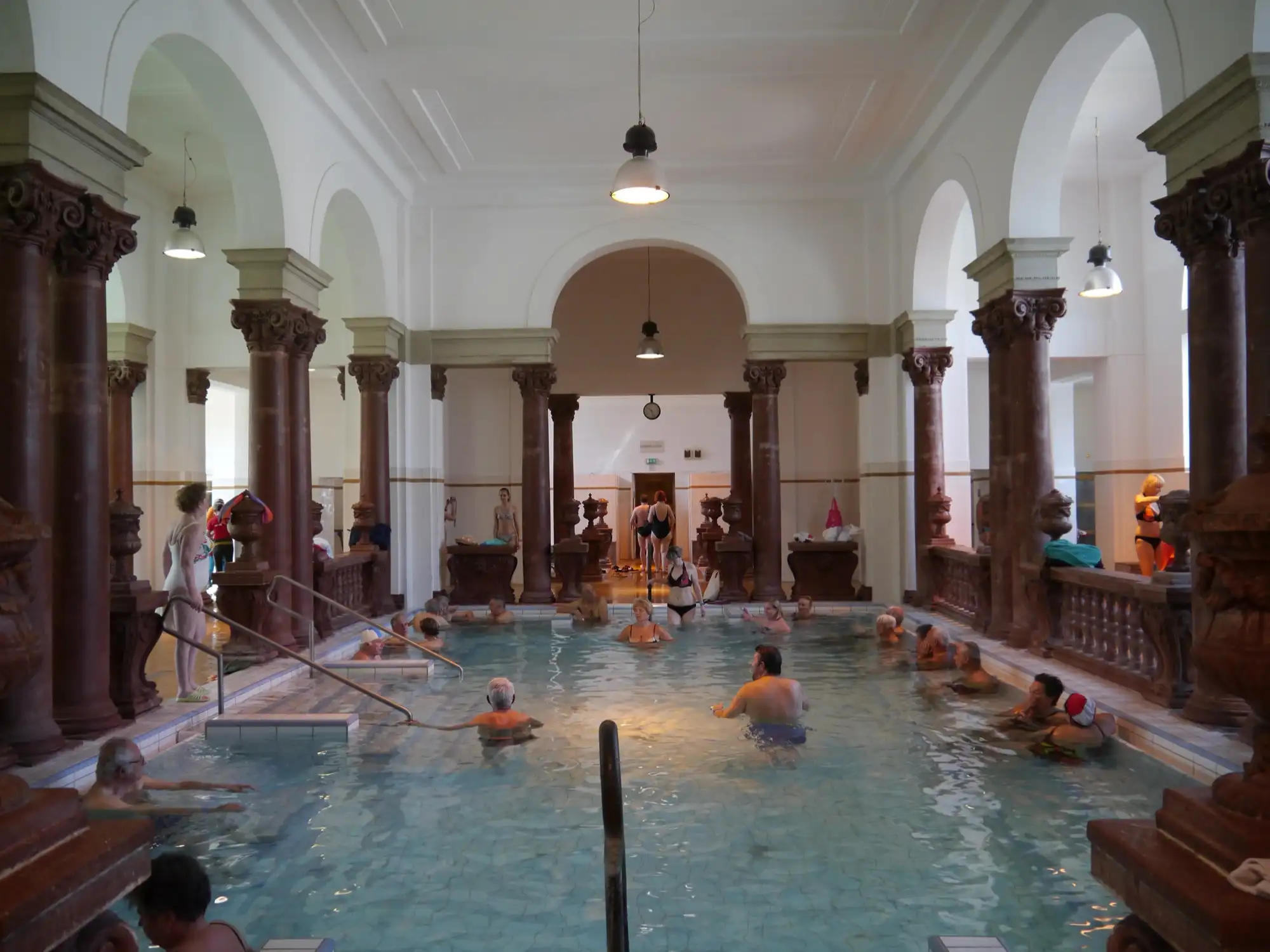 Bathers in an indoor thermal pool at Széchenyi Thermal Bath, under arches on red marble columns