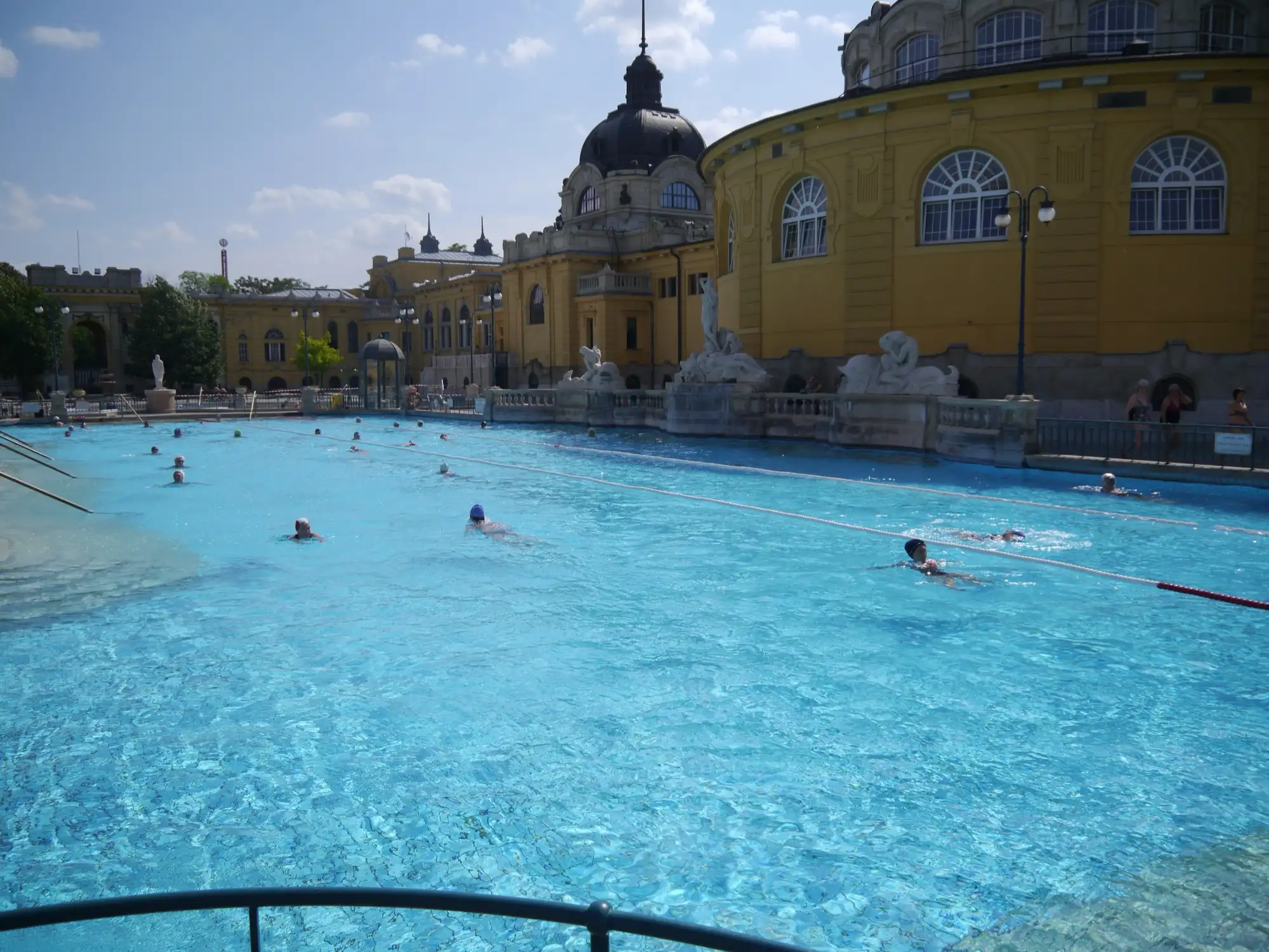 Outdoor pool in front of the yellow wings and dome of Széchenyi Thermal Bath, Budapest
