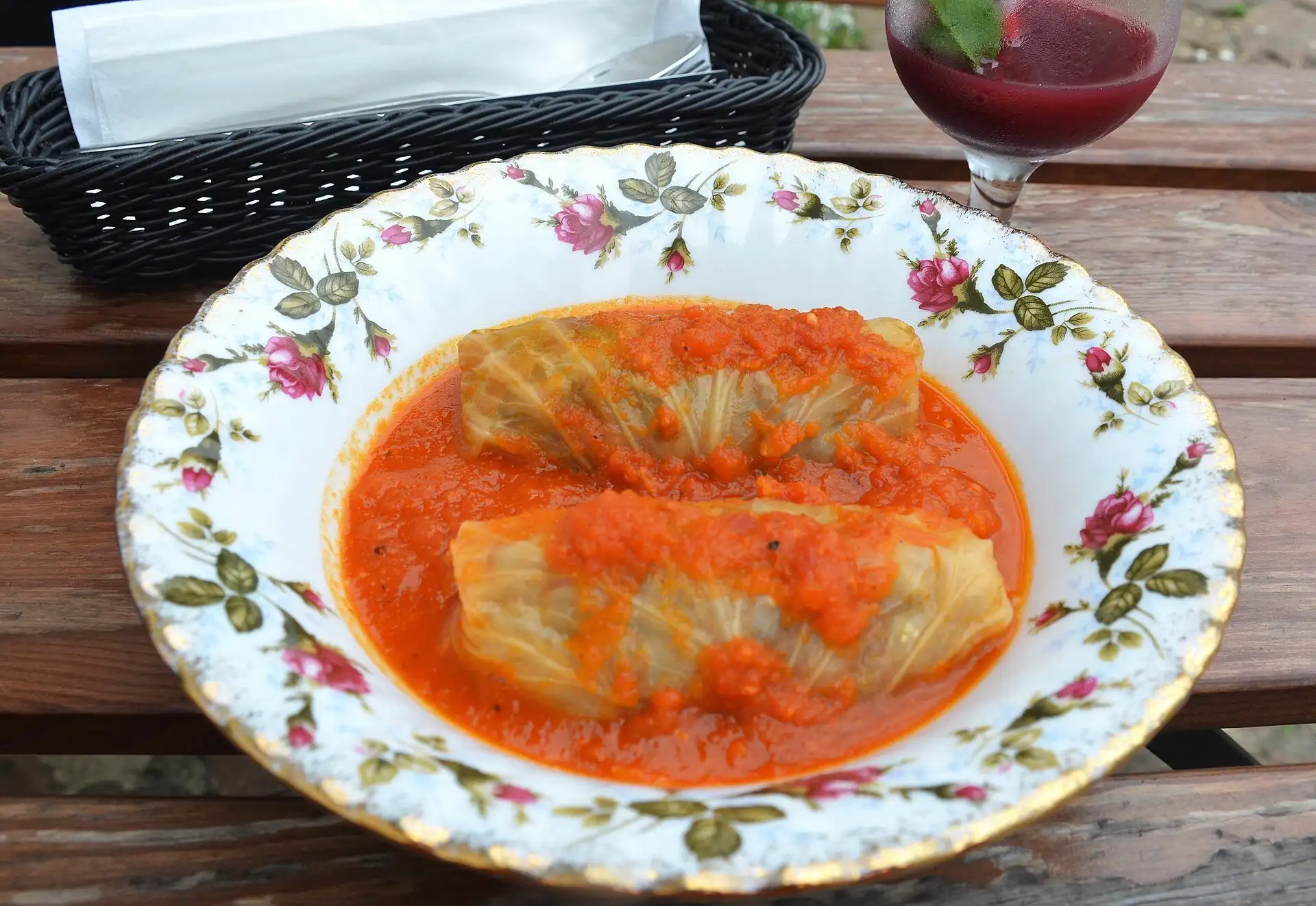 Two Hungarian stuffed cabbage rolls in pickled cabbage leaves, in tomato sauce on a plate with a pink rose pattern, on a wooden table