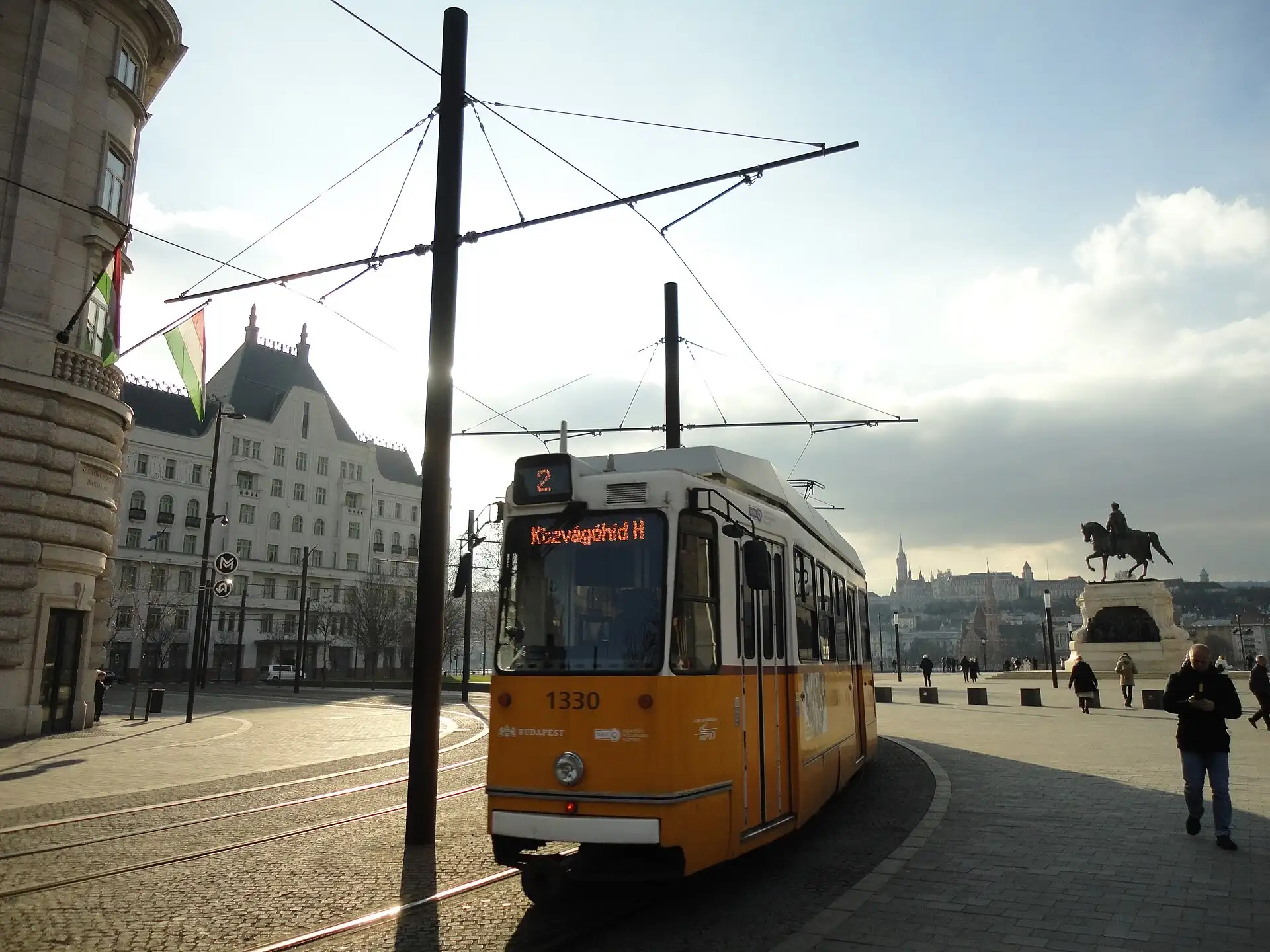 A yellow number 2 tram on Kossuth Lajos tér in Budapest, with Matthias Church and Fisherman's Bastion across the Danube behind it