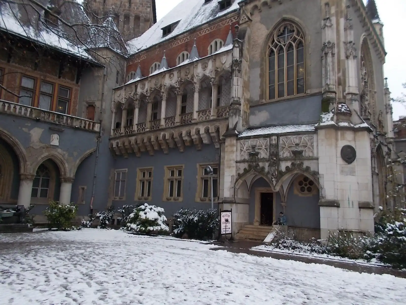 The Gothic north facade of the Hunyadi courtyard at Vajdahunyad Castle in Budapest under snow, with its traceried windows and stone arcade