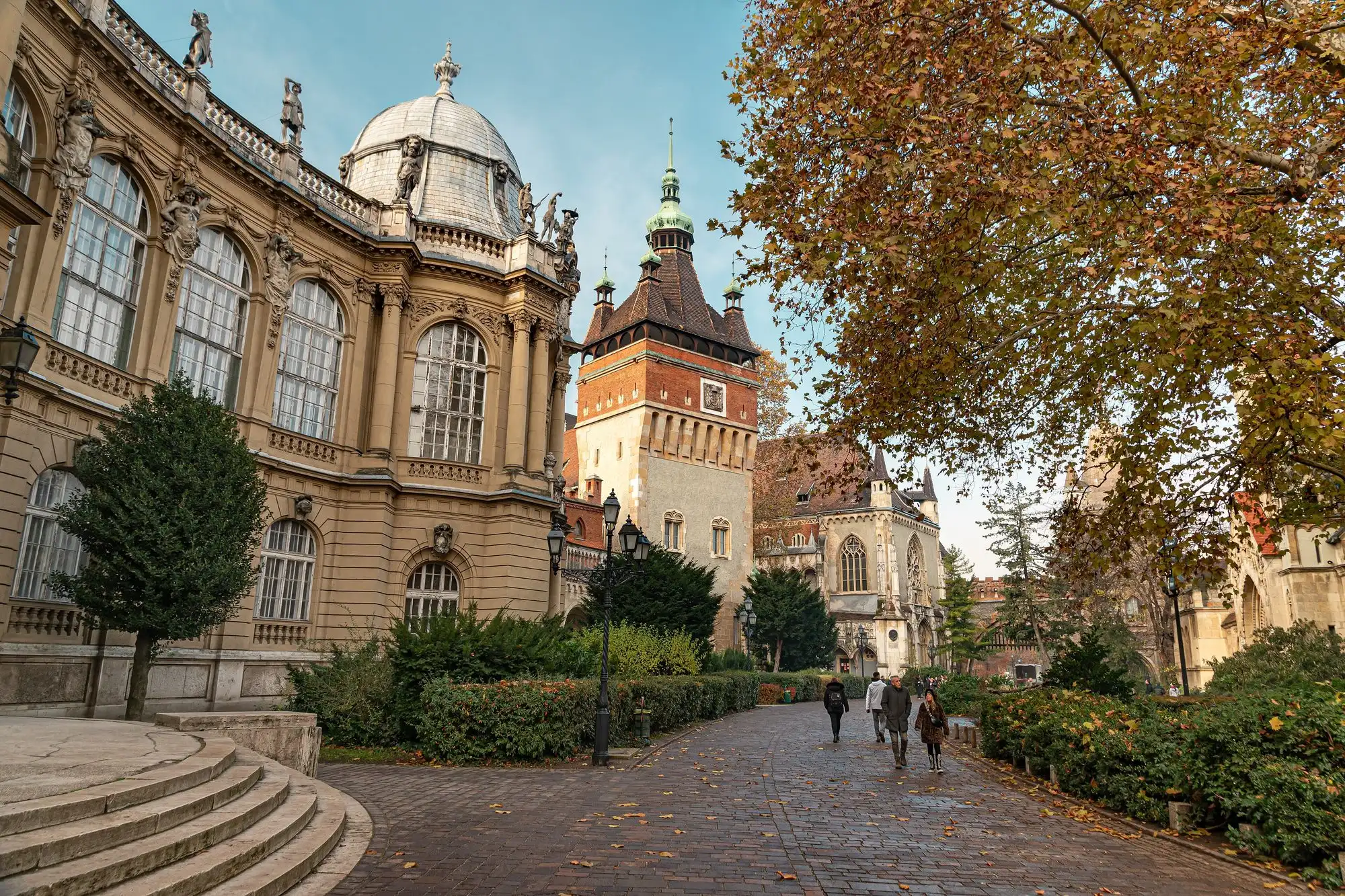 Visitors on the steps in front of Vajdahunyad Castle in Budapest's City Park, with the castle's ornate facade and towers rising behind autumn trees