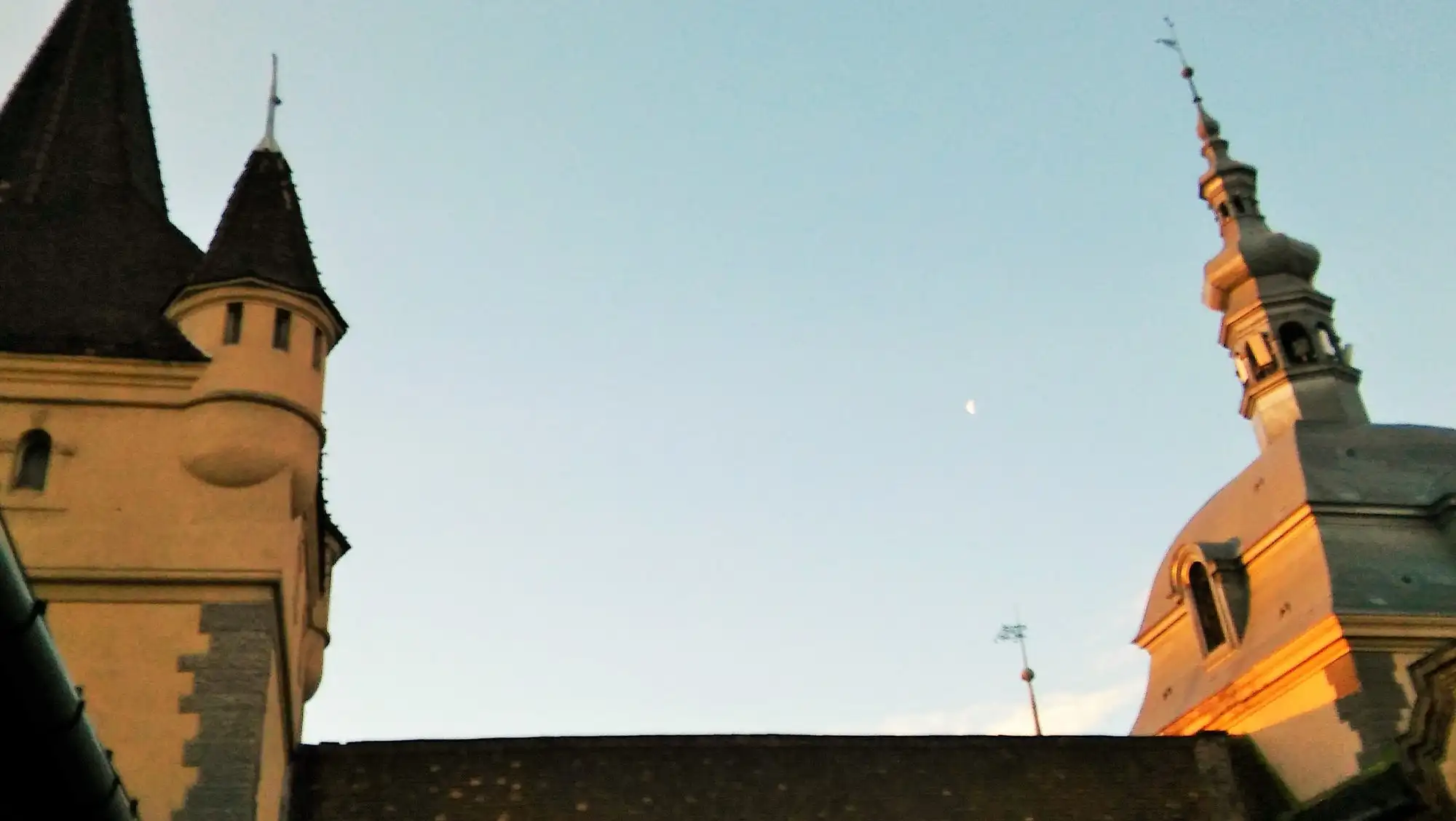 The towers and spires of Vajdahunyad Castle in Budapest against a clear sky, the Gothic Apostles' Tower and the castle's steep tiled roofs