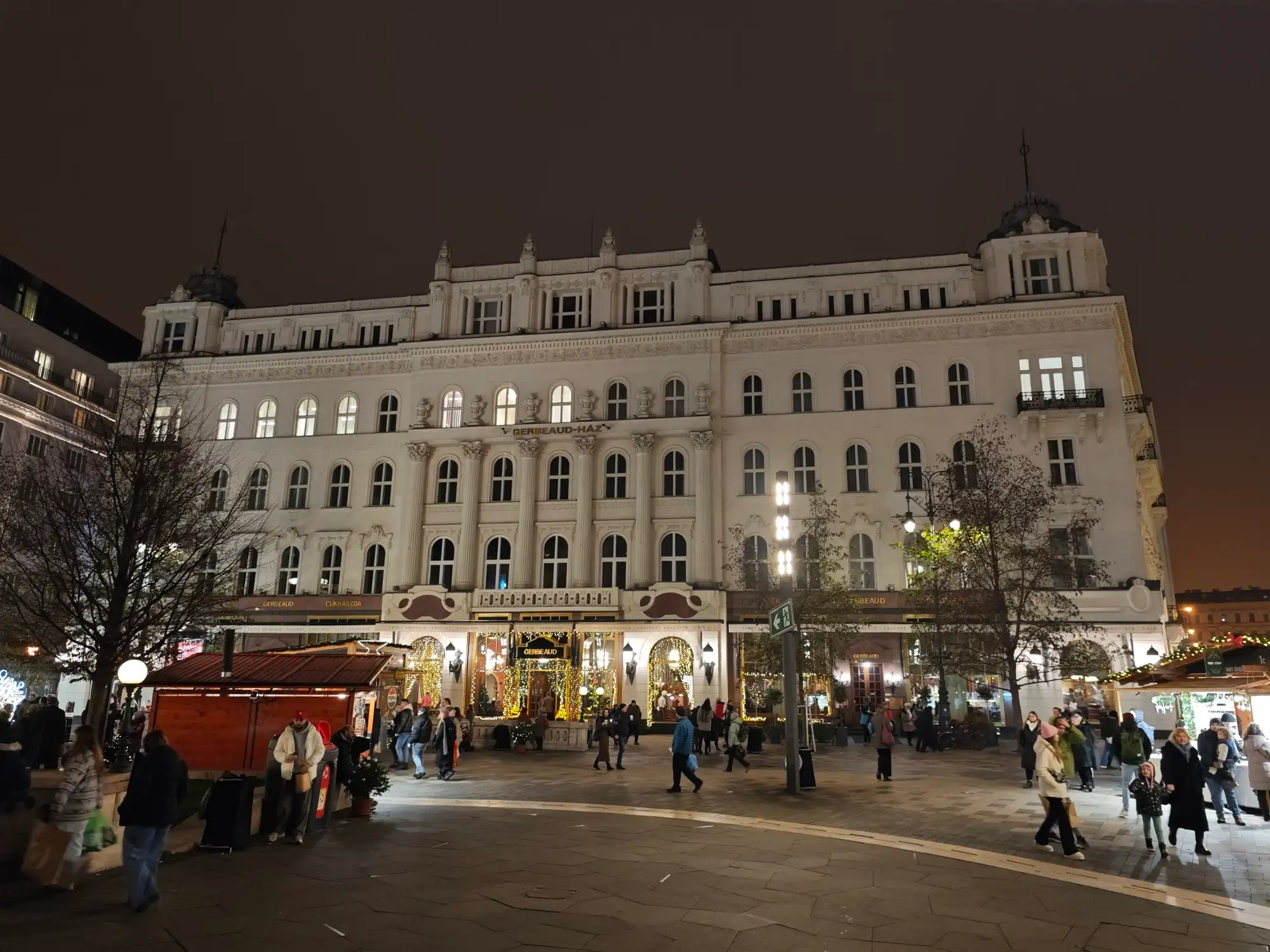 The Gerbeaud building lit up at night on the north side of Vörösmarty tér, with Christmas market stalls in front