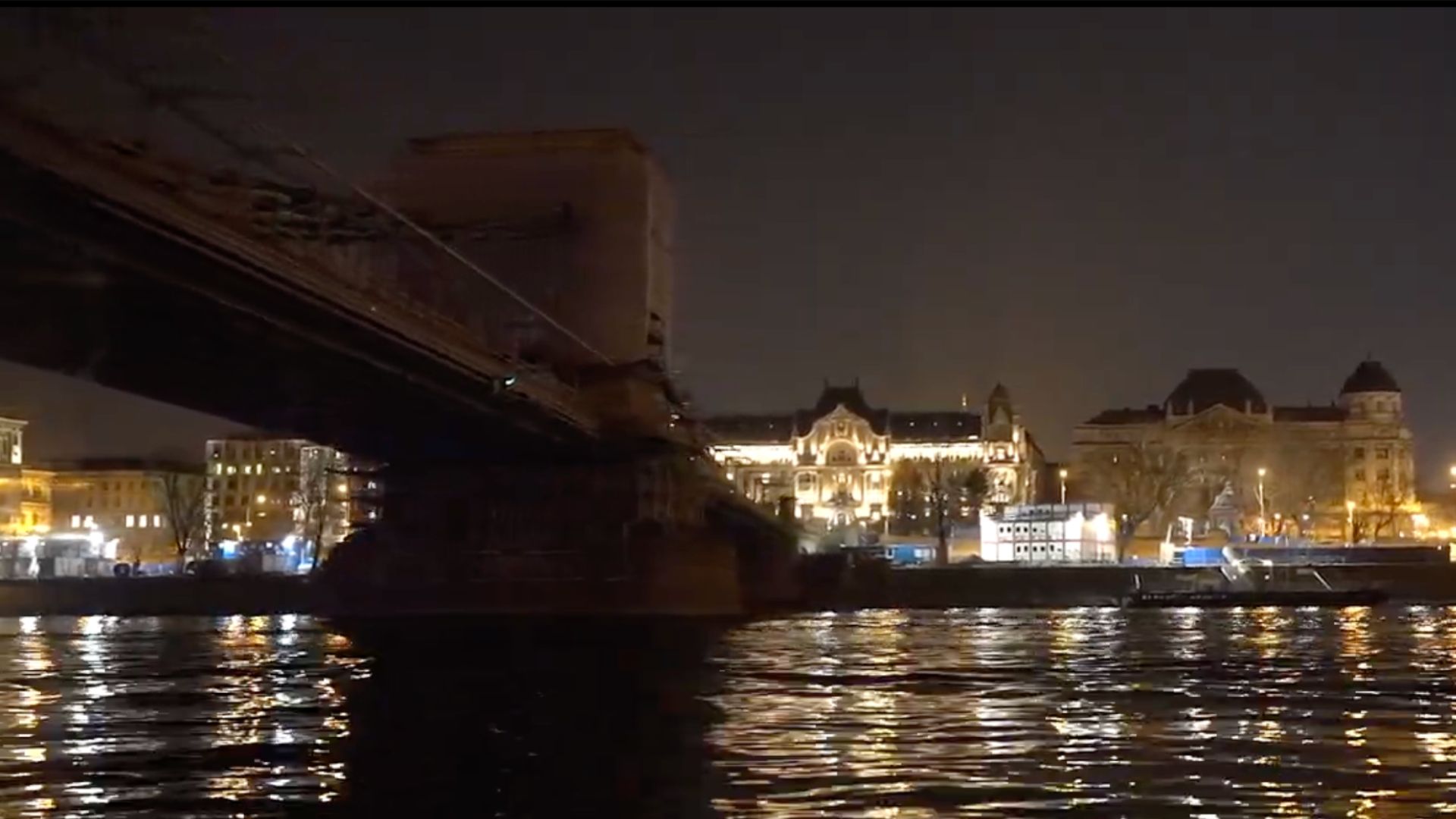 Night view of the Chain Bridge in Budapest with illuminated buildings reflecting on the Danube River.