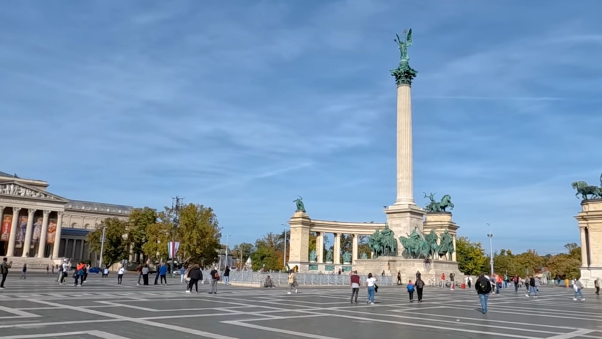 View of the central monument at Heroes' Square in Budapest, with people walking around the square.