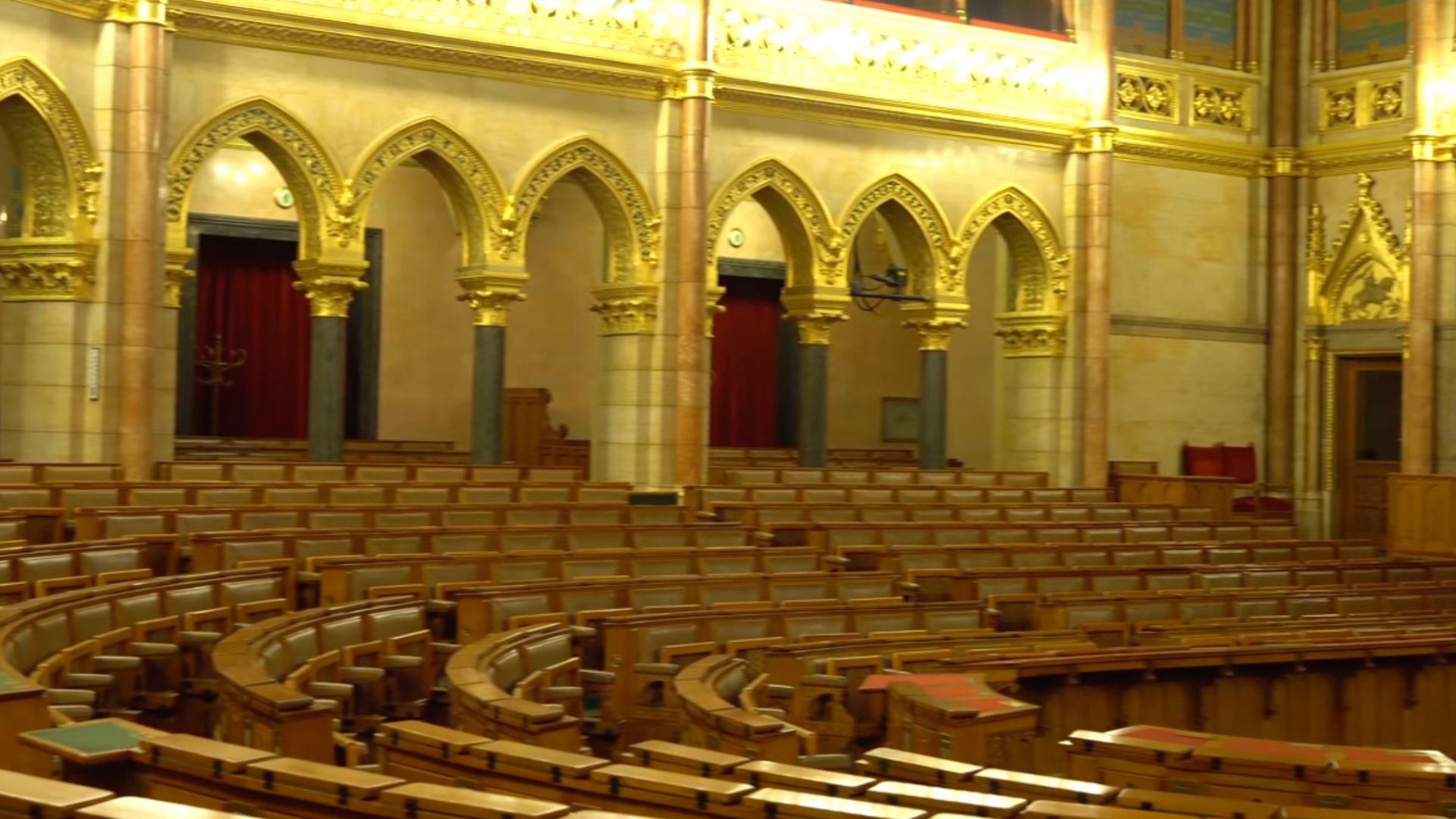 Hungarian Parliament Building interior view of the main assembly hall with rows of wooden seats, golden arches, and ornate decorations.