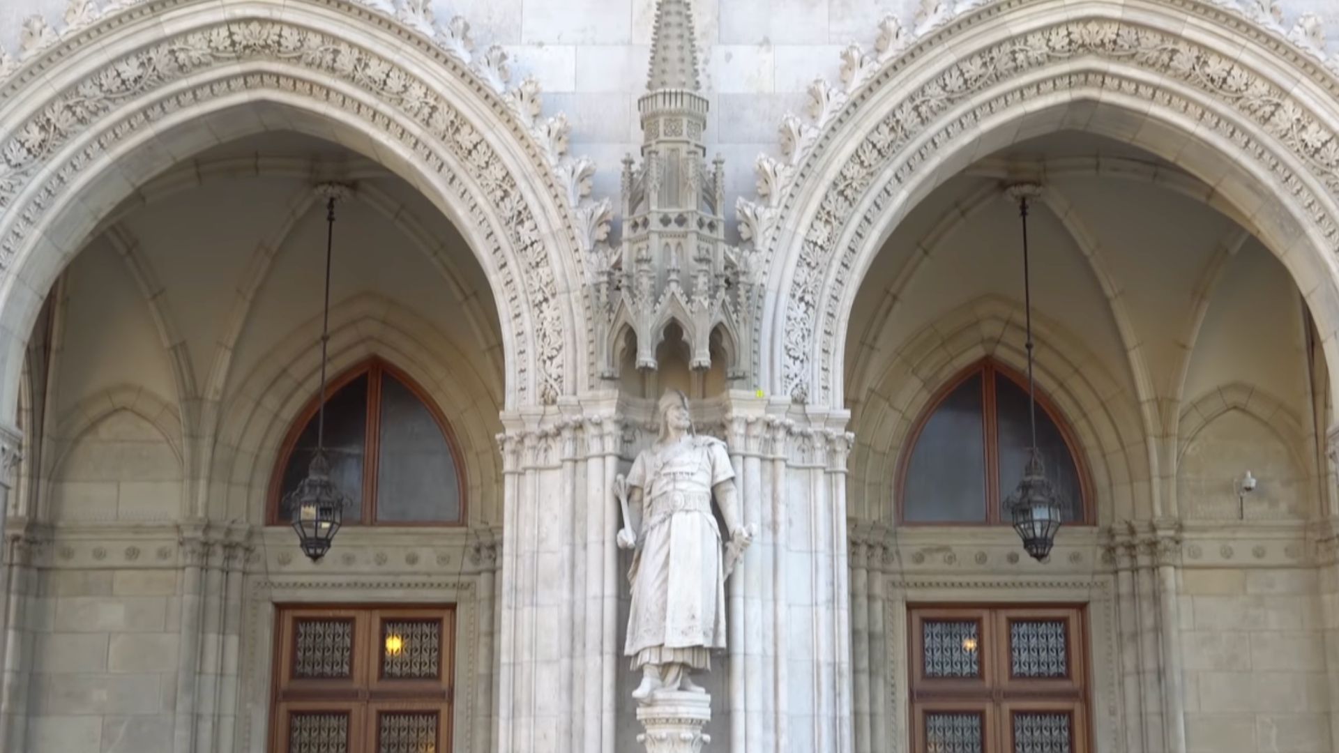 Hungarian Parliament Building entrance featuring a detailed statue of a historical figure set between two arched doorways with gothic architectural elements.