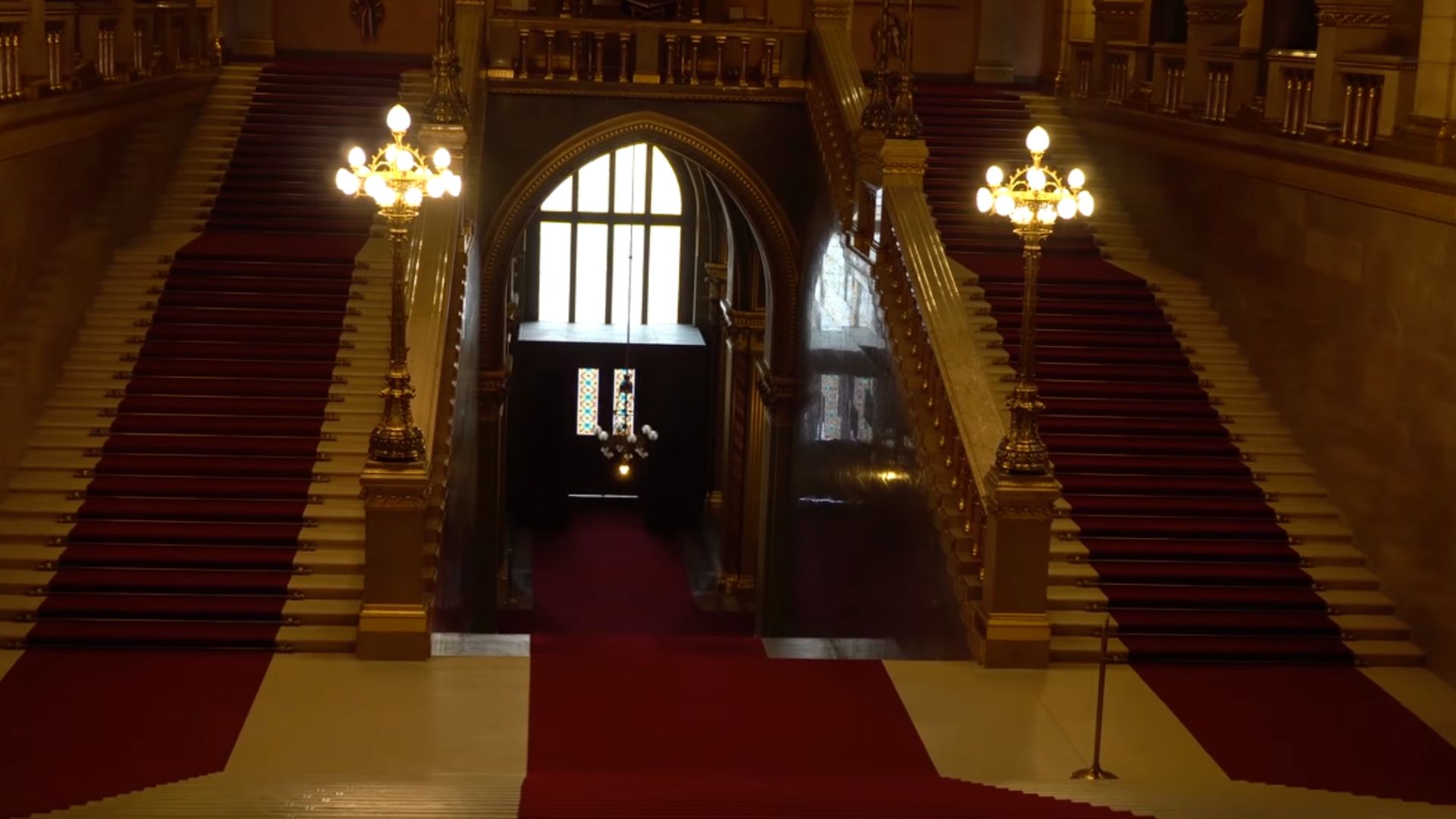 Hungarian Parliament Building grand staircase illuminated with golden lights, showcasing intricate architectural details and red carpets.