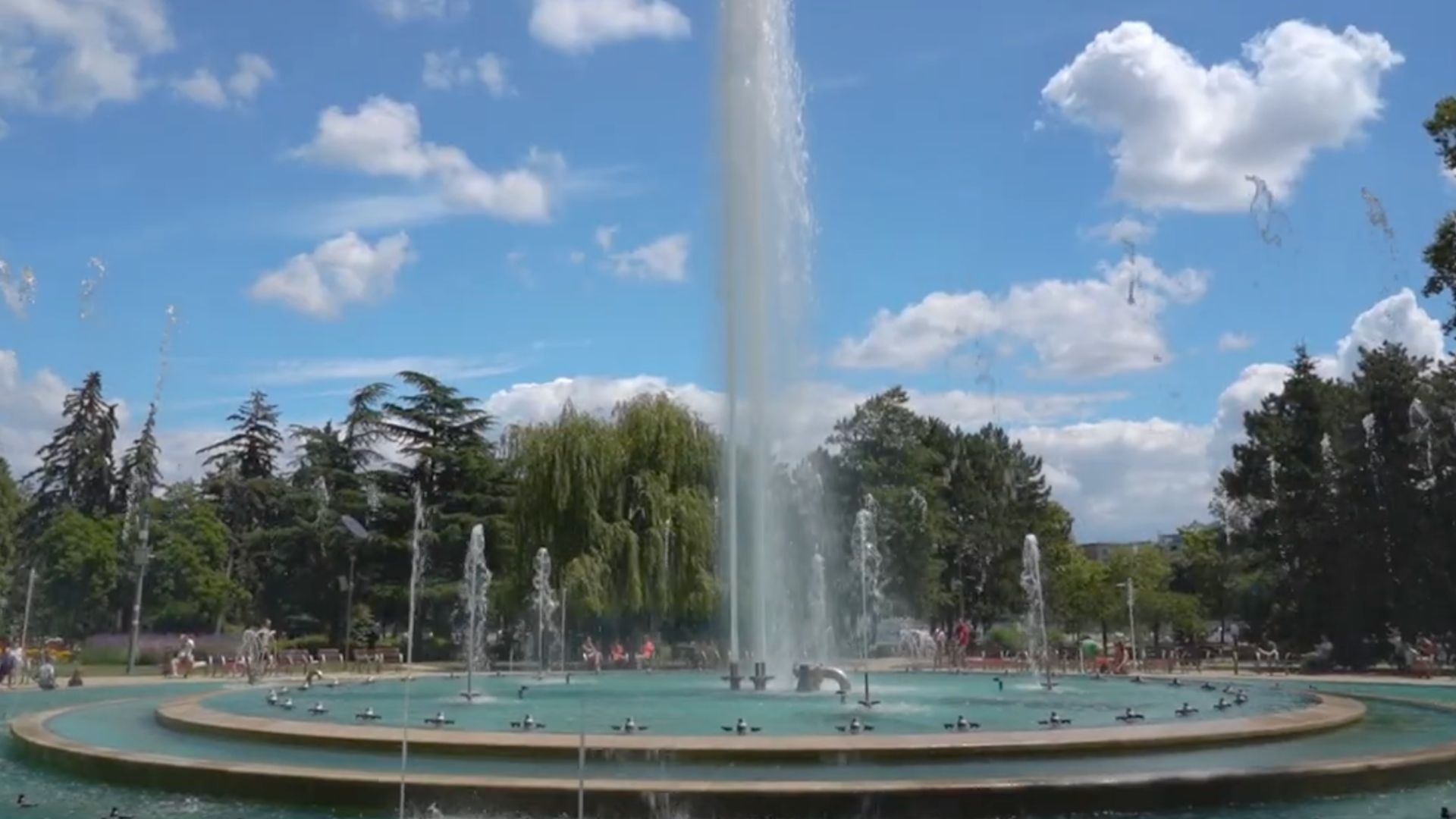 A large musical fountain on Margaret Island in Budapest, on a sunny day with people and trees in the background.
