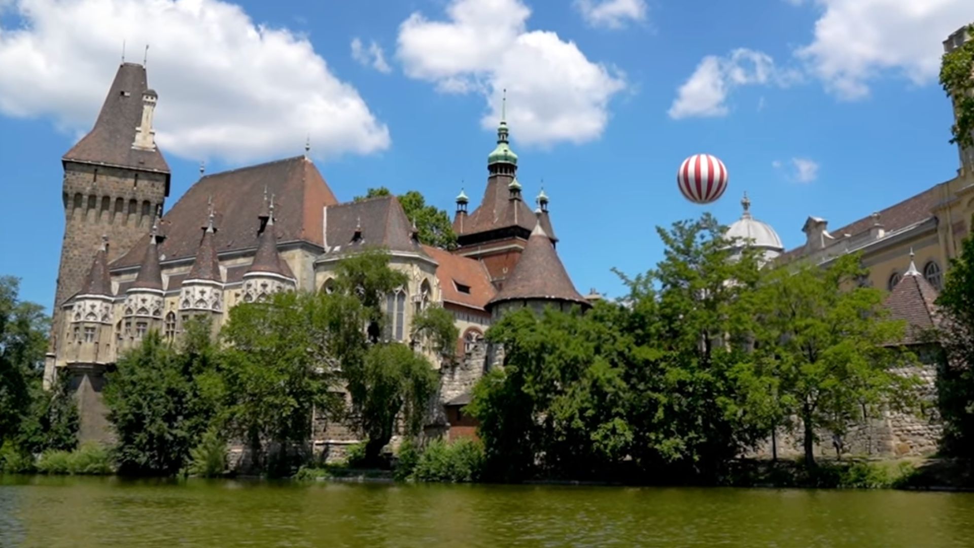 View of Vajdahunyad Castle in Budapest with a hot air balloon in the background.