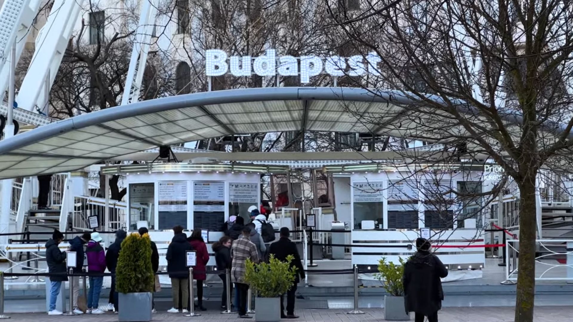 Budapest Eye ticket booth with people waiting in line, and the "Budapest" sign visible above the booth.