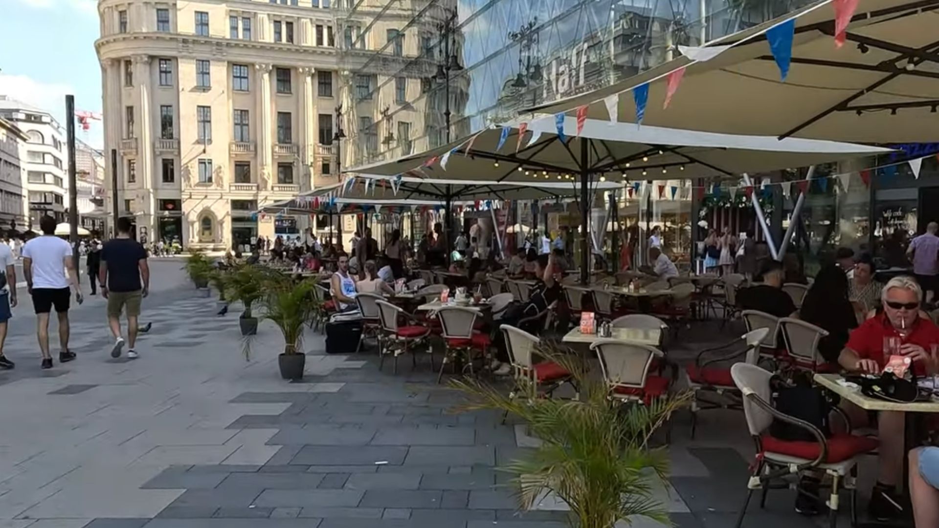 utdoor café in Budapest with people dining under canopies, colorful bunting above, and historic buildings in the background.