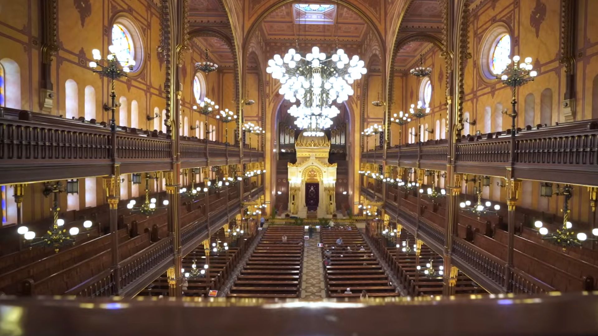 Interior of the Dohány Street Synagogue in Budapest, featuring rows of wooden pews, large chandeliers, and the beautifully detailed ark at the front.