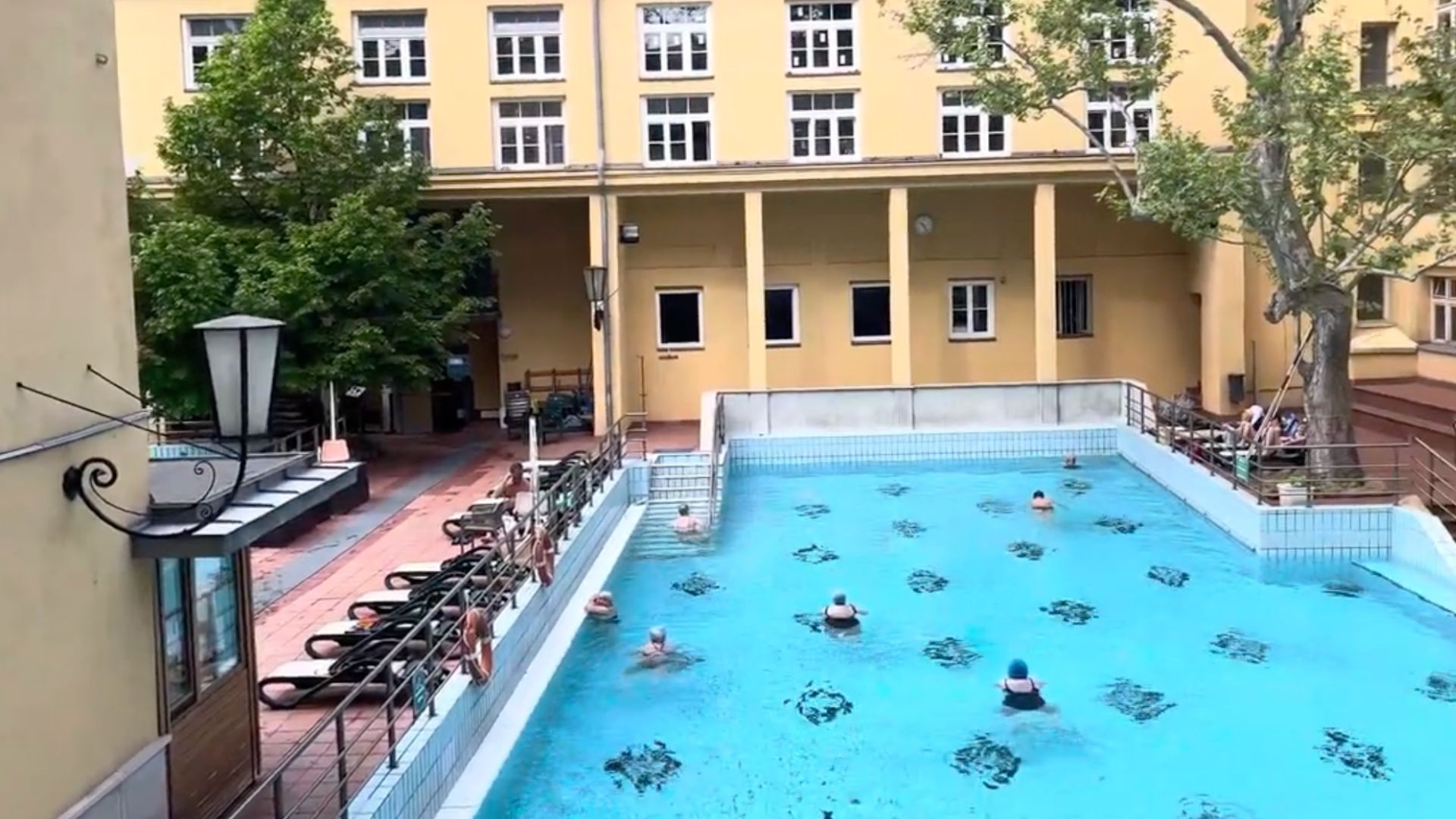 Swimming pool at Lukács Thermal Bath in Budapest, with a few people swimming and others relaxing by the side.