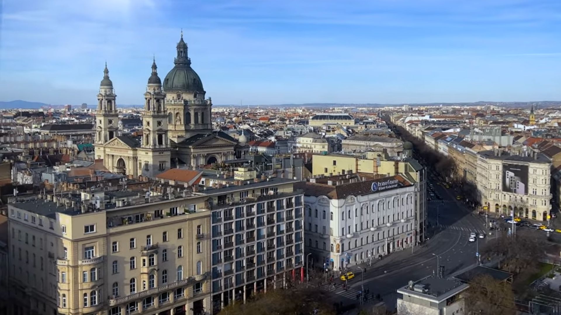 Aerial view of St. Stephen's Basilica from the Budapest Eye in Budapest, with surrounding cityscape under a clear blue sky.