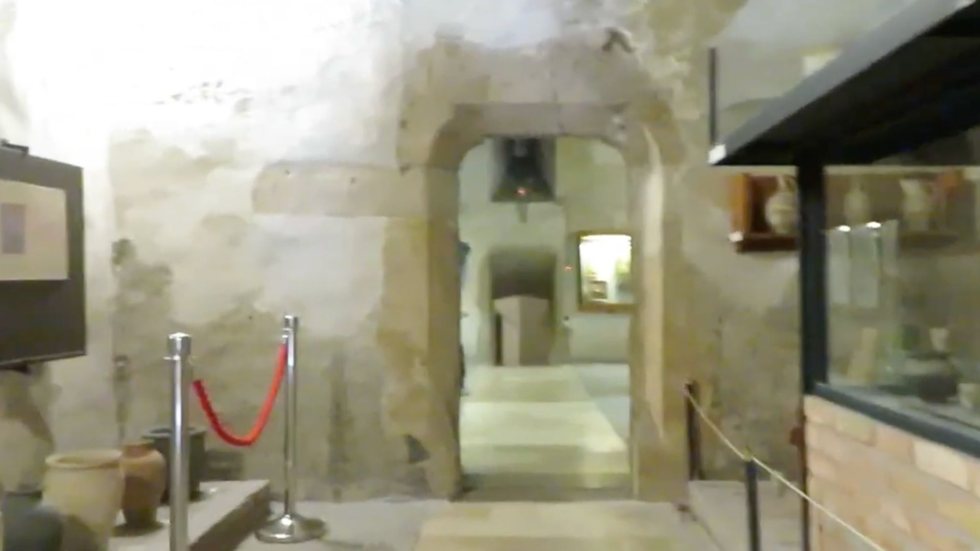 Narrow hallway with stone walls inside the Budapest History Museum, featuring historical artifacts and a roped-off exhibit area.